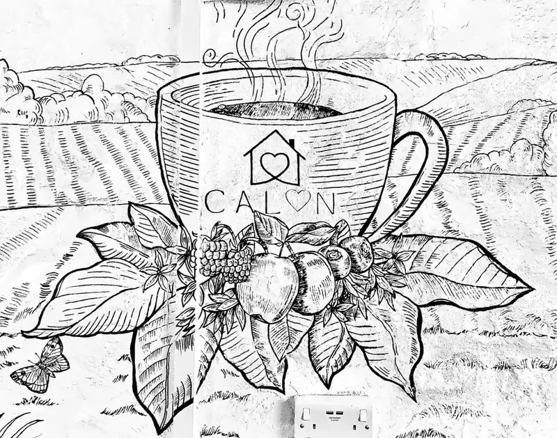 Katy Rose's black-ink botanical mural illustration of the Calon coffee cup surrounded by Isle of Wight hills, berries and leaves