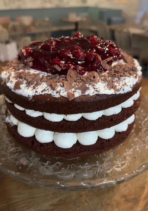 Three-layer homemade chocolate cherry gateau topped with cherry compote and chocolate curls