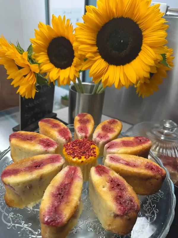 Freshly baked homemade raspberry friands adorned with cheerful yellow sunflower blossoms on the counter at Calon