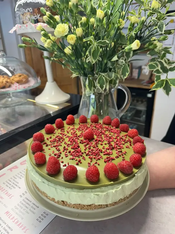 Homemade pistachio cheesecake topped with fresh raspberries and freeze-dried raspberry crumb on the counter